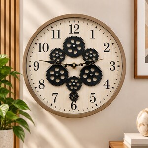 May include: A round wall clock with a light wood-toned frame and a cream-colored face. The clock features black Arabic numerals and a central arrangement of six interconnected black mechanical gears. Two slender black hands indicate the time.