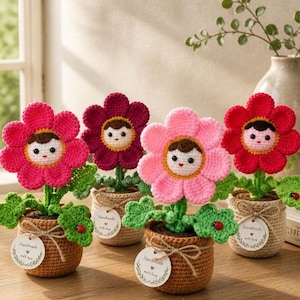 May include: Four crocheted flower figures in brown pots, each with a central face and brown hair. The flowers have petals in shades of hot pink, dark purple, light pink, and red. Each pot features a round tag reading Handmade with love.