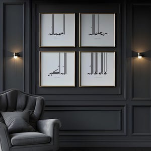 May include: A set of four square wall art prints in thin gold frames, each featuring black Arabic calligraphy on a white background with vertical line accents. The prints are arranged in a two-by-two grid on a dark grey panelled wall.