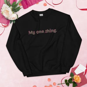 Könnte beinhalten: Ein schwarzes Langarm-Sweatshirt mit Rundhalsausschnitt und dem Text My one thing. in einem dunkelroten und violetten Farbverlauf mittig auf der Brust. Das Kleidungsstück hat einen gerippten Kragen, Bündchen und Saum in Standardpassform.