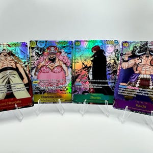 Op de afbeelding: Vier holografische One Piece ruilkaarten met Edward Newgate, Charlotte Linlin, Shanks en Kaido. Elke kaart toont een karakterillustratie, een kostprijs van 10, een kracht van 12000 en gedetailleerde speltekst op een reflecterend oppervlak.