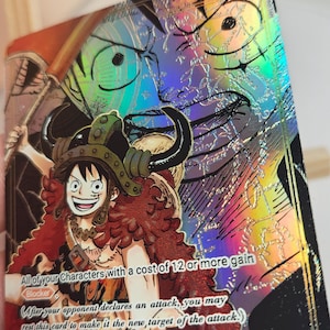 May include: A holographic trading card featuring Monkey D. Luffy wearing a horned helmet and a red cape. The card displays the text 'All of your Characters with a cost of 12 or more gain Blocker' and 'After your opponent declares an attack, you may rest this card'.