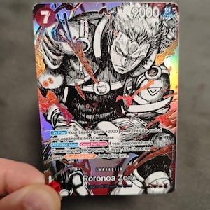 Peut inclure: Une carte à collectionner One Piece holographique représentant Roronoa Zoro dans une illustration en noir et blanc style encre. La carte affiche un niveau de puissance de 9000, un coût de 7 et inclut du texte de jeu détaillé sur les capacités.