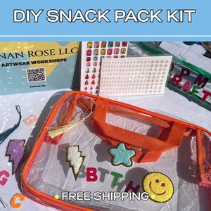 May include: A clear plastic pouch with orange trim and handles, featuring a gold tassel and various colorful patches including a star, lightning bolt, and smiley face. The kit includes sheets of adhesive gems and pearls for DIY decoration.