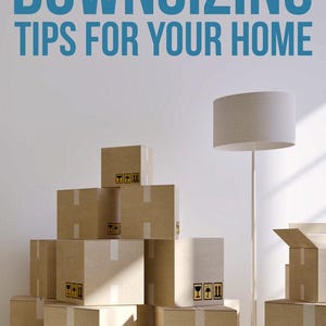 May include: A stack of brown cardboard moving boxes with white tape and black fragile symbols, positioned next to a tall white floor lamp. The text DOWNSIZING TIPS FOR YOUR HOME is printed in large blue letters at the top of the image.