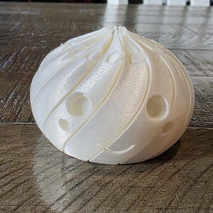 May include: A white, spherical, 3D-printed object with a swirling, ribbed texture and small, circular indentations distributed across its surface. The object has a pointed top and a rounded base, featuring a smooth, matte finish throughout its structure.