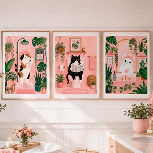 Puede incluir: Un conjunto de tres láminas decorativas enmarcadas con gatos en un baño rosa. La primera muestra un gato calicó duchándose, la segunda un gato blanco y negro leyendo en el inodoro y la tercera un gato blanco frente a un espejo con plantas.