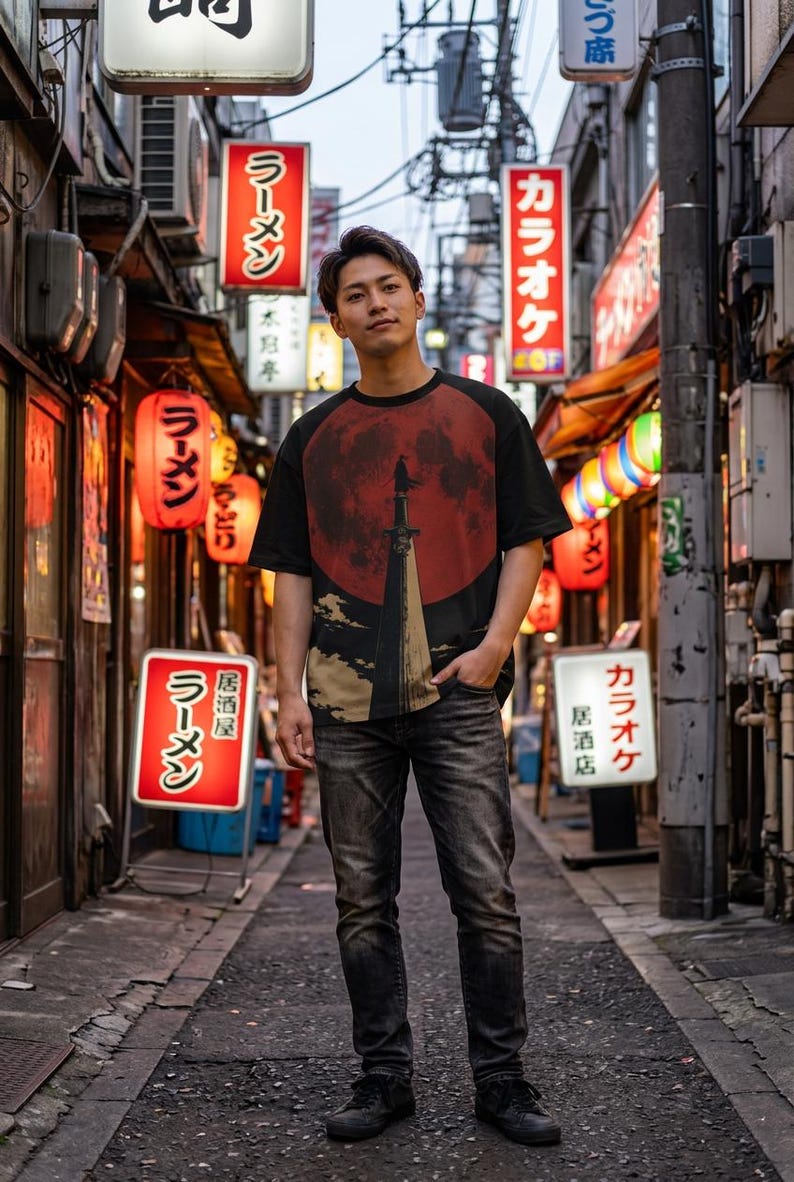 May include: A black short-sleeved t-shirt featuring a graphic print of a dark silhouette standing atop a tall pillar against a large red moon, paired with dark grey denim jeans and black sneakers, worn in a narrow urban alleyway with signs.