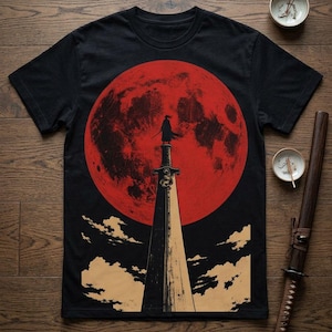 May include: A black short-sleeve t-shirt featuring a graphic print of a silhouette standing atop a sword handle against a large red moon. The design includes stylized clouds at the base of the sword, creating a high-contrast scene on the fabric.