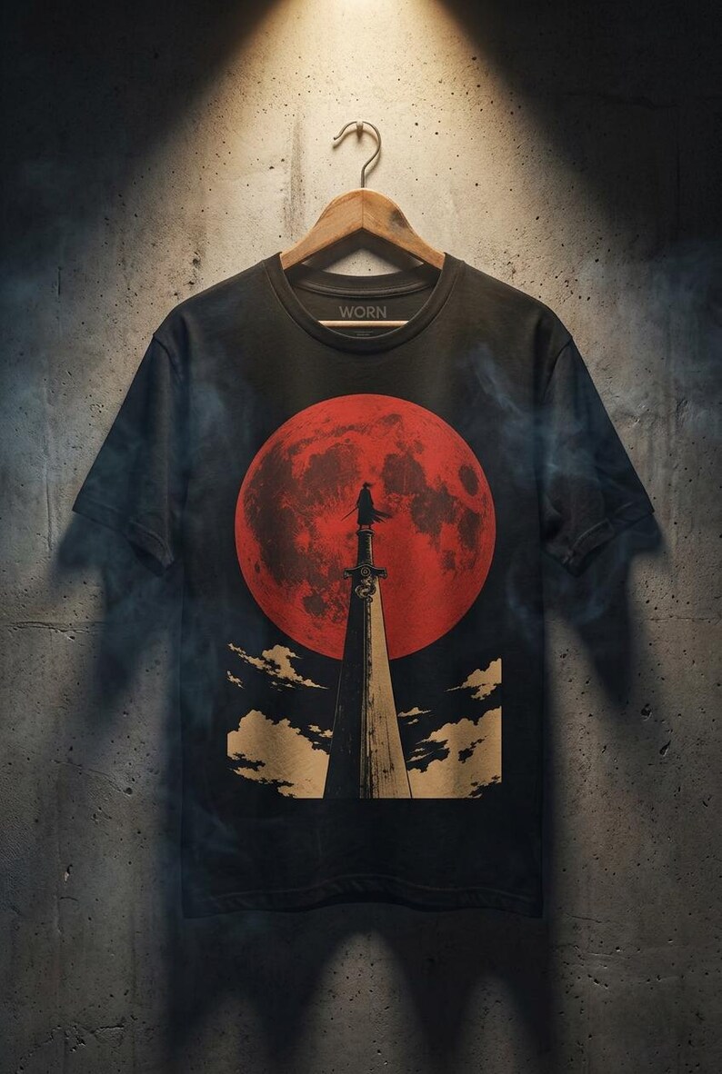 May include: A black short-sleeve t-shirt featuring a graphic print of a figure standing atop a tall, pointed structure against a large, textured red moon. The design includes stylized clouds at the base and the word WORN printed inside the neck collar.