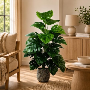 May include: A tall artificial monstera plant with large, deep green, split leaves. The plant is housed in a dark, textured cylindrical pot featuring a repeating golden leaf pattern. The foliage is dense and upright, showcasing the iconic fenestrations.