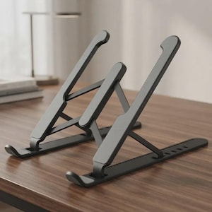 May include: A matte black adjustable laptop stand featuring two angled support arms with hooked ends to secure a device. The frame is constructed with a collapsible, open-structure design, including a notched base rail for multiple height settings.