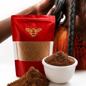 May include: A red stand-up pouch with a gold bee logo containing a brown powder, accompanied by a white bowl filled with the same brown powder and a small pile of the powder on the surface. The pouch features a clear window showing the contents.