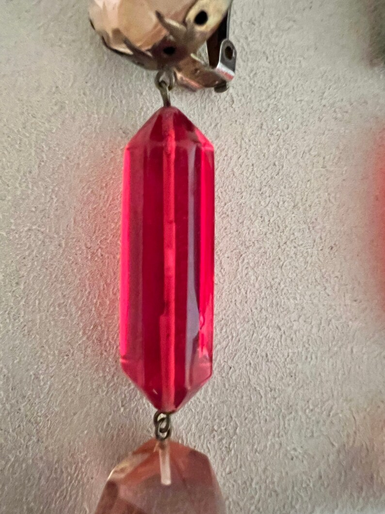 May include: A pair of vintage earrings with a red faceted glass teardrop pendant and a clear faceted glass teardrop pendant. The earrings are attached to a silver clip-on earring.