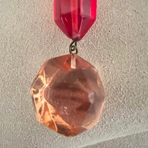 May include: A red glass prism with a faceted, clear glass orb hanging from it. The orb is a light brown color.