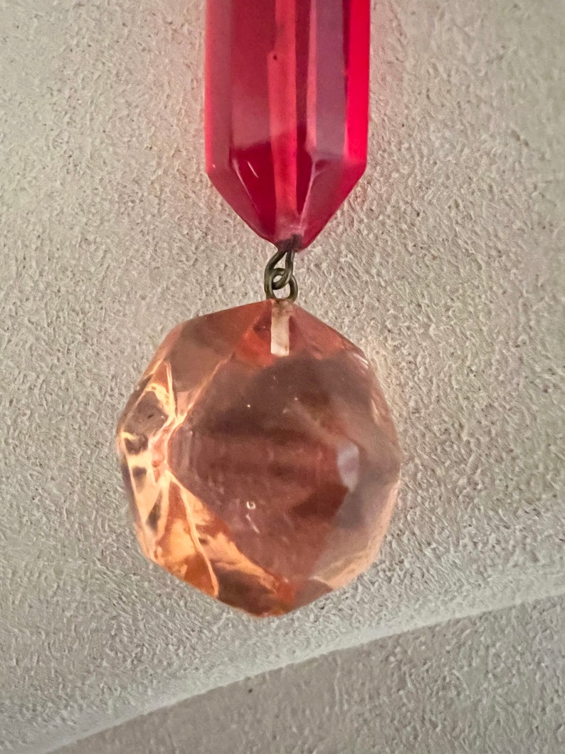 May include: A red glass prism with a faceted, clear glass orb hanging from it. The orb is a light brown color.