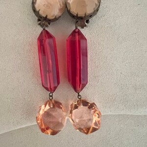 May include: A pair of dangle earrings with a clear, faceted crystal top, a red, faceted crystal drop, and a smaller, clear, faceted crystal at the bottom.