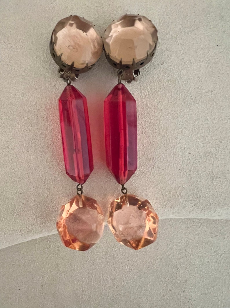 May include: A pair of dangle earrings with a clear, faceted crystal top, a red, faceted crystal drop, and a smaller, clear, faceted crystal at the bottom.