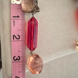 May include: A pair of dangle earrings with a red faceted crystal and a peach-colored faceted crystal. The earrings are approximately 3 inches long.