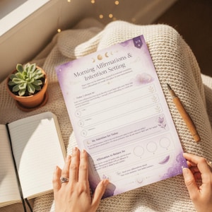May include: A printed sheet titled Morning Affirmations & Intention Setting with purple watercolor accents, moon phases, and floral illustrations. The page includes sections for daily intentions, numbered lists for affirmations, and three circular checkboxes.