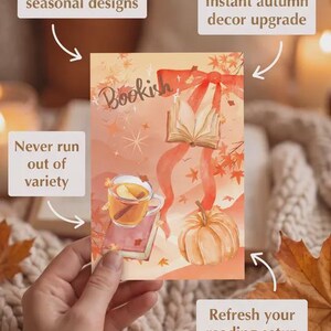 Puede incluir: Una impresión rectangular con la palabra Bookish en letra cursiva, un libro abierto con una cinta roja, una taza de cristal con una bebida caliente y una calabaza. El diseño incluye hojas de otoño y estrellas sobre un fondo naranja suave.