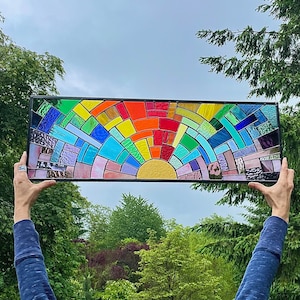 May include: A stained glass window depicting a rainbow arch with a yellow sun in the center. The rainbow is made up of individual pieces of glass in various shades of red, orange, yellow, green, blue, indigo, and violet.