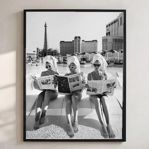 Könnte beinhalten: Ein schwarz-weiß gerahmter Wandkunstdruck, der drei Personen mit weißen Handtüchern auf dem Kopf und Sonnenbrillen zeigt, die Zeitungen an einem Swimmingpool vor der Skyline von Las Vegas mit dem Eiffelturm-Nachbau und Hotelgebäuden lesen.
