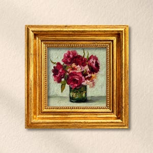 May include: An oil painting of a bouquet of deep red and pink peonies in a green glass vase, presented in a thick, ornate gold-colored frame with a beaded inner edge. The artwork features visible brushstrokes and a textured, light-colored background.