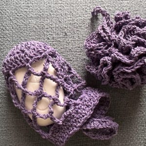 May include: Two purple crocheted soap savers. One is a net-like pouch with a bar of soap inside. The other is a round, fluffy ball.