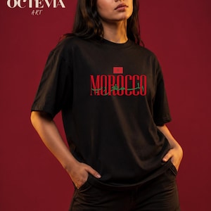 Peut inclure: Un t-shirt noir à manches courtes arborant le mot MOROCCO en lettres capitales rouges, surmonté du drapeau marocain et accompagné d'une inscription en arabe de couleur verte. Le motif est centré sur la poitrine du vêtement.