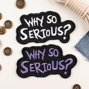 May include: Two black embroidered patches with a scalloped edge, each featuring the text "WHY SO SERIOUS?" in a stylized font. One patch has white embroidery, while the other patch features the same text in a light purple thread color.