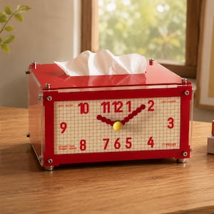Könnte beinhalten: Ein rechteckiger Taschentuchbox-Halter aus rotem Acryl mit einem Zifferblatt-Design auf der Vorderseite. Das Zifferblatt hat einen weißen Rasterhintergrund mit roten Zahlen von 1 bis 12, roten Uhrzeigern und einem gelben Mittelpunkt.
