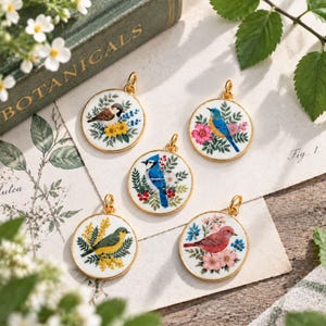 May include: Five circular gold-rimmed pendants featuring detailed illustrations of birds and flowers. Each pendant displays a different bird species, including a blue jay, a red bird, and a yellow bird, surrounded by colourful botanical elements.