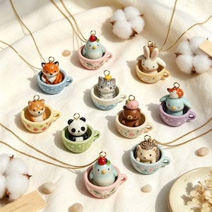 May include: A collection of ten gold-tone chain necklaces featuring miniature ceramic animal pendants, each sitting inside a small, colorful, patterned teacup. The animals include a fox, panda, bear, rabbit, hedgehog, and various birds.