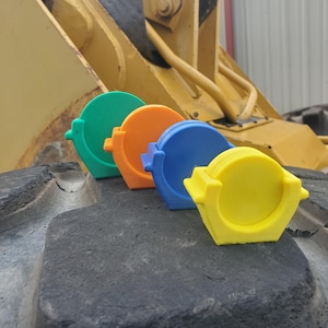 May include: Four circular, stand-up holders in green, orange, blue, and yellow. Each holder features a flat base and a central circular recessed area, arranged in a diagonal line. The objects are constructed from a solid, matte-finish material.