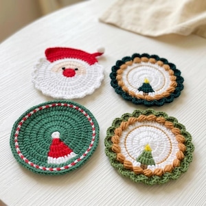 May include: Four circular crochet coasters featuring holiday designs. One depicts a Santa face with a red hat, one is green with a red and white hat, and two feature white centers with small green Christmas trees and textured borders in green and brown.