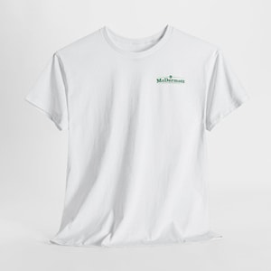 May include: A white short-sleeve t-shirt featuring a crew neckline and a small green graphic logo on the upper left chest area. The logo consists of the text McDermott in a green serif font with a small emblem centered above the word.