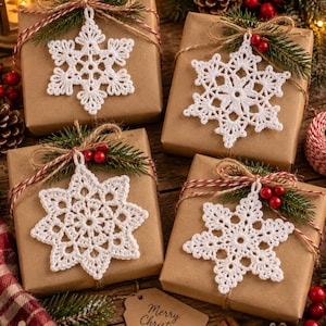 May include: Four square gift boxes wrapped in brown paper, each adorned with a white crocheted snowflake ornament, a sprig of green pine needles, red berries, and red and white twine. A brown paper gift tag with the text Merry Christmas is included.