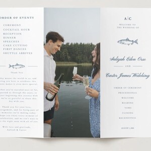May include: A tri-fold wedding programme featuring a central photograph of two people holding champagne glasses by a lake. The left panel lists the order of events and a thank you note. The right panel displays the names Aaliyah Eden Orso and Carter James Wedeking, a fish illustration, and the order of ceremony.