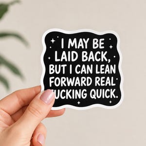 May include: A black, wavy-edged sticker with white text that reads: I MAY BE LAID BACK, BUT I CAN LEAN FORWARD REAL FUCKING QUICK. The design includes small white star accents scattered across the black background and a thin white border.