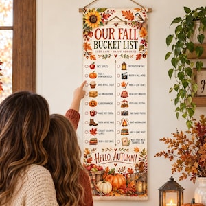 May include: A vertical fabric wall hanging titled Our Fall Bucket List with a wooden dowel and rope. The banner features autumn-themed illustrations like sunflowers, pumpkins, and leaves, alongside a checklist of seasonal activities and text.