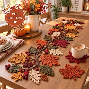 May include: A crochet table runner featuring a vine of autumn leaves in shades of orange, red, yellow, green, and cream, accented with small berries. The set includes matching leaf-shaped coasters and a PDF pattern label in the upper left corner.