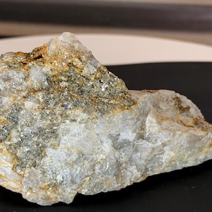 May include: A raw mineral specimen featuring a combination of translucent white quartz crystals and patches of metallic, dark grey to bronze-colored pyrite inclusions. The rock has an irregular, jagged shape with a rough, crystalline texture throughout.