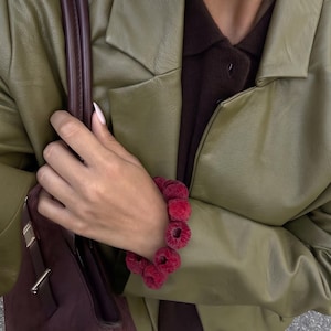 Könnte beinhalten: Ein olivgrüner Blazer aus Kunstleder über einem dunkelbraunen Hemd mit Kragen, kombiniert mit einer tiefburgunderroten Wildlederhandtasche und einem Armband aus einer Reihe frischer roter Himbeeren am Handgelenk.