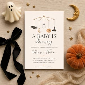 Może przedstawiać: Prostokątne zaproszenie na baby shower z kremowym tłem, ozdobione ilustracją karuzeli z nietoperzem, księżycem, duszkiem, dynią i kapeluszem czarownicy. Tekst głosi A BABY IS Brewing, na cześć Olivii Thomas, w sobotę 9 października o 14:00.