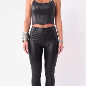 May include: A black faux leather crop top with a rhinestone-trimmed neckline and matching black faux leather skinny pants. The outfit is accessorized with large square sunglasses, a wide rhinestone choker, silver bangles, and black high-heeled sandals.