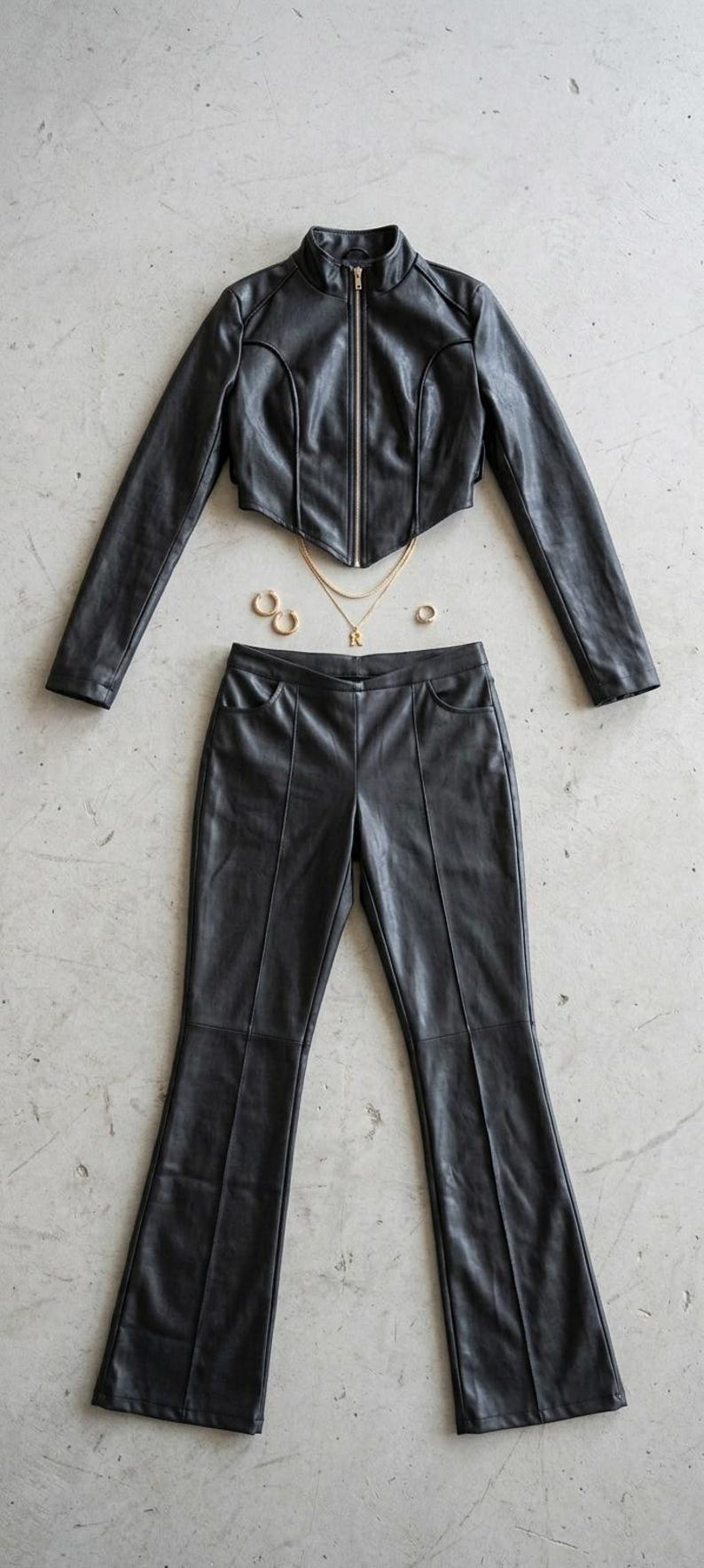 Black faux leather two-piece women’s outfit featuring a cropped zip-up jacket with stand collar and panel stitching, paired with matching high-waist flared pants, styled for edgy streetwear and modern fashion.