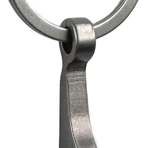 May include: A silver-toned metal bottle opener keychain featuring a circular split ring attached to a slender, curved handle with a notched hook design at the bottom for prying off bottle caps. The entire object has a smooth, brushed finish.