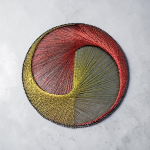 Può includere: Un'opera d'arte circolare realizzata con fili tesi che presenta un motivo geometrico creato con fili metallici rossi e dorati avvolti attorno a un perimetro di piccoli spilli neri. I fili si incrociano formando un design curvo e vorticoso.