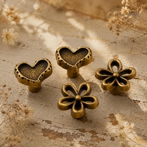 May include: Four antique brass cabinet knobs featuring two heart-shaped designs with textured centers and two flower-shaped designs with open petals. Each knob has a metallic finish and a central mounting post for attachment to furniture.
